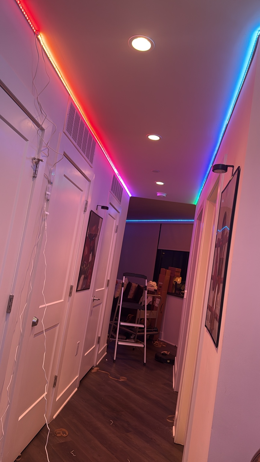 Multicolor LED strips along a hallway ceiling during installation, with tools and a ladder visible.